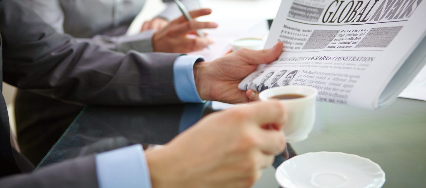 Businessman with newspaper having coffee at workplace